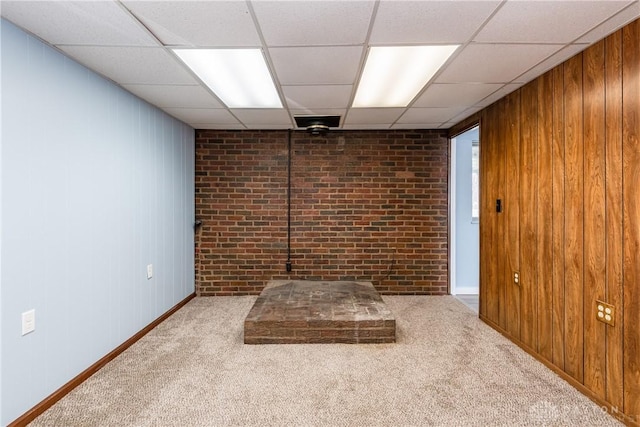 unfurnished room featuring a paneled ceiling, wooden walls, and carpet floors