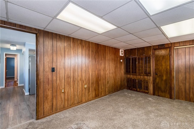 carpeted spare room with a drop ceiling and wooden walls