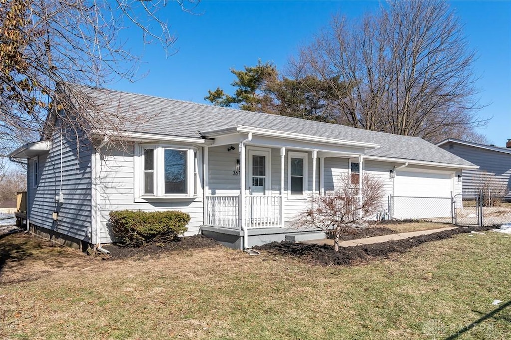 view of front facade with a front yard, covered porch, roof with shingles, and an attached garage