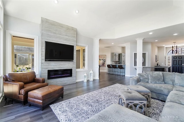 living room with dark hardwood / wood-style floors, a large fireplace, and ornate columns