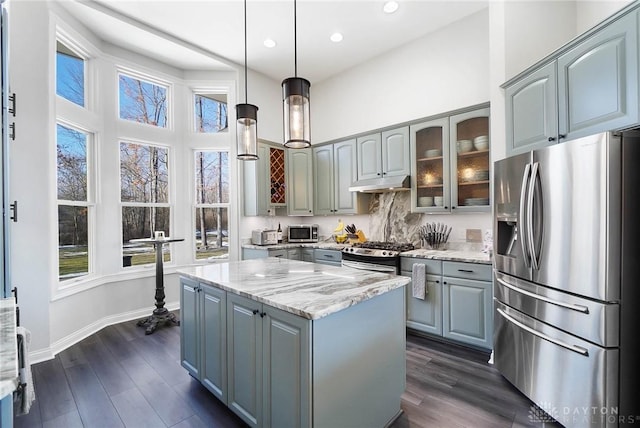 kitchen with a kitchen island, appliances with stainless steel finishes, dark hardwood / wood-style floors, hanging light fixtures, and light stone counters