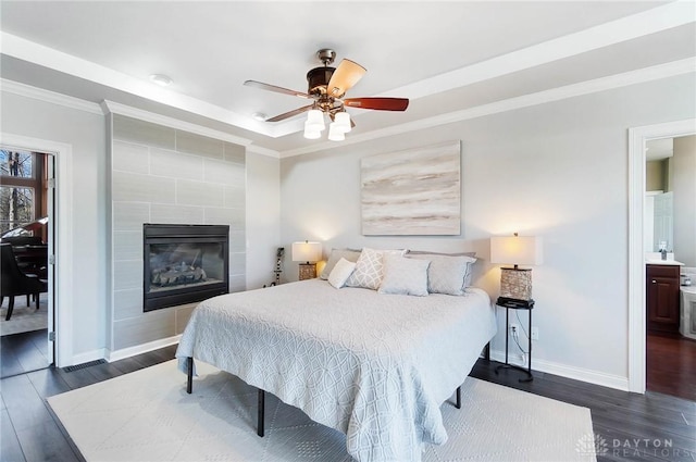 bedroom featuring dark wood-type flooring, a tile fireplace, ceiling fan, a tray ceiling, and ornamental molding