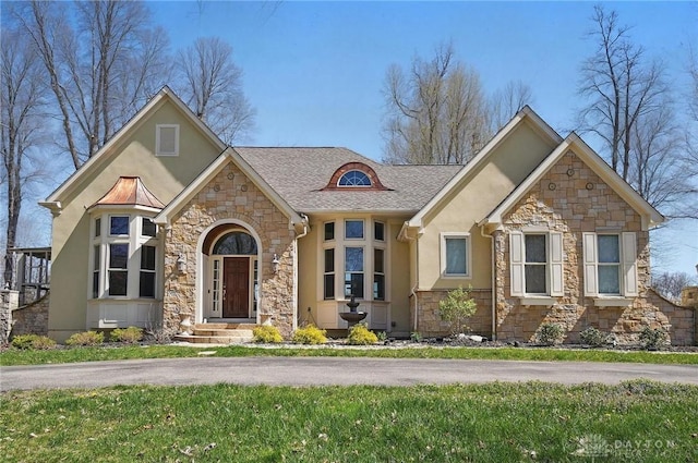 view of front facade with roof with shingles, stucco siding, a front yard, and stone siding