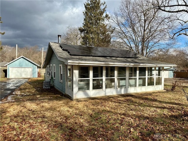 back of property with a lawn, a garage, a sunroom, solar panels, and an outbuilding