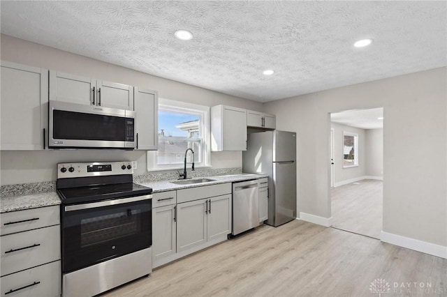 kitchen featuring sink, stainless steel appliances, light stone counters, a textured ceiling, and light wood-type flooring