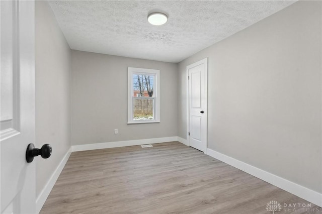 spare room with a textured ceiling and light hardwood / wood-style flooring