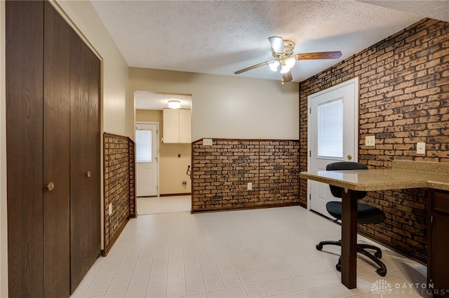 office area featuring ceiling fan, brick wall, and a textured ceiling