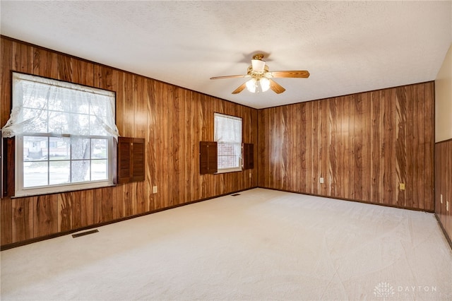 carpeted empty room featuring ceiling fan, a textured ceiling, and wood walls