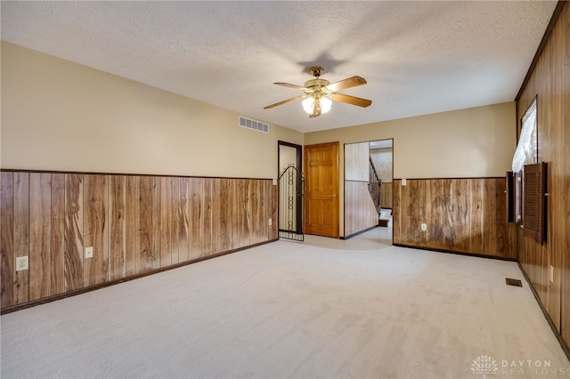 spare room featuring ceiling fan, wooden walls, light colored carpet, and a textured ceiling