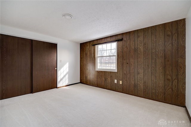 unfurnished bedroom with light carpet, a closet, a textured ceiling, and wood walls