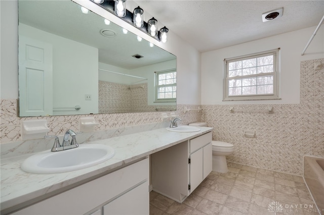 bathroom with vanity, toilet, a textured ceiling, and tile walls