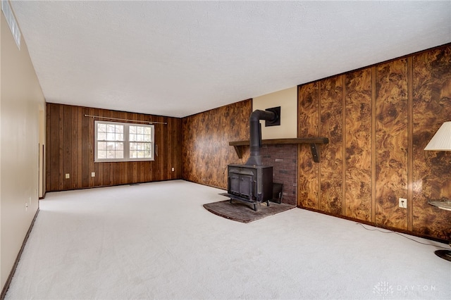 unfurnished living room featuring light colored carpet, wood walls, a textured ceiling, and a wood stove