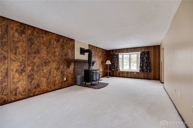 unfurnished living room featuring wooden walls, light colored carpet, and a wood stove