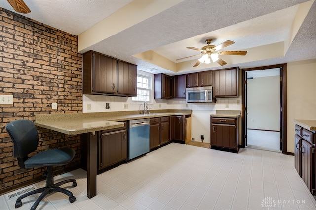 kitchen with appliances with stainless steel finishes, sink, a raised ceiling, dark brown cabinets, and a textured ceiling