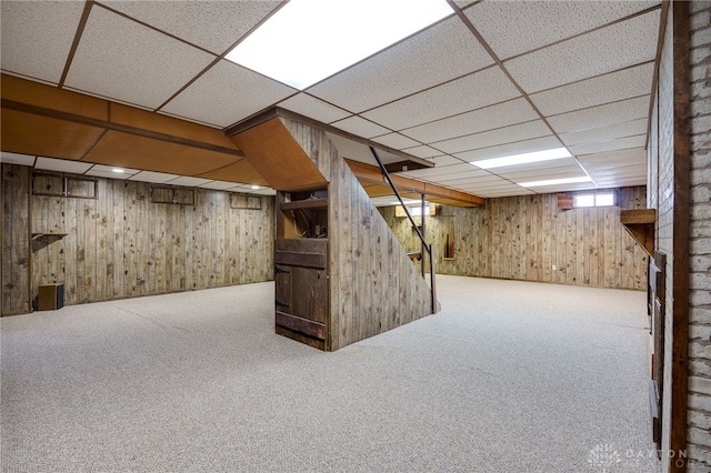 basement with carpet flooring, a paneled ceiling, and wooden walls