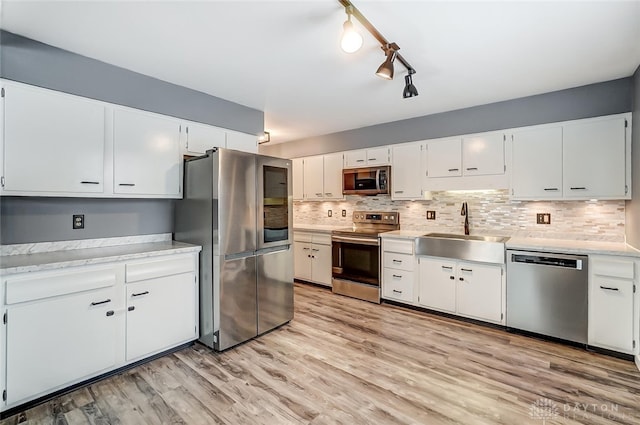 kitchen with sink, white cabinetry, light hardwood / wood-style flooring, stainless steel appliances, and decorative backsplash