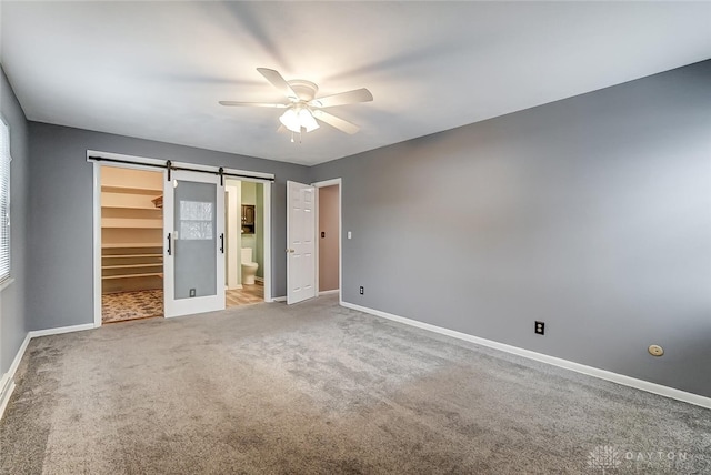 unfurnished bedroom featuring a walk in closet, ensuite bath, carpet floors, a closet, and a barn door