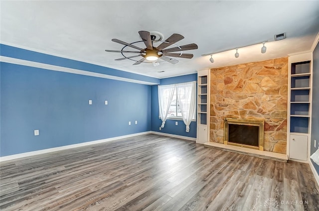 unfurnished living room featuring hardwood / wood-style flooring, ceiling fan, a stone fireplace, and built in shelves