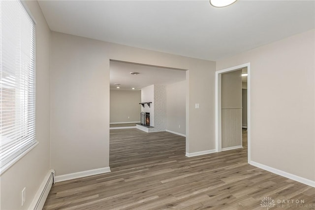 spare room with hardwood / wood-style flooring, a baseboard radiator, and a brick fireplace