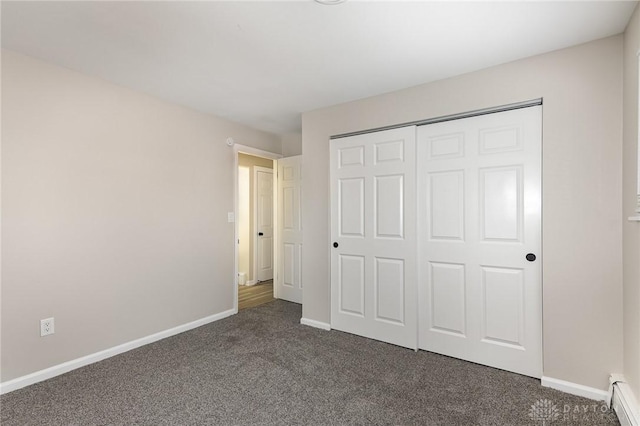 unfurnished bedroom with baseboard heating, dark carpet, and a closet