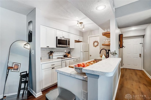 kitchen with a breakfast bar area, a textured ceiling, white appliances, decorative backsplash, and white cabinets