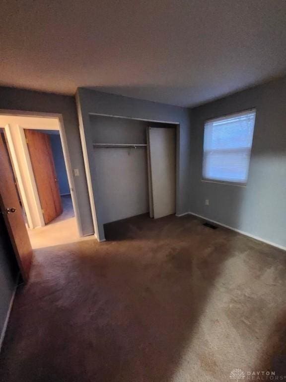 unfurnished bedroom featuring a textured ceiling, a closet, and dark colored carpet