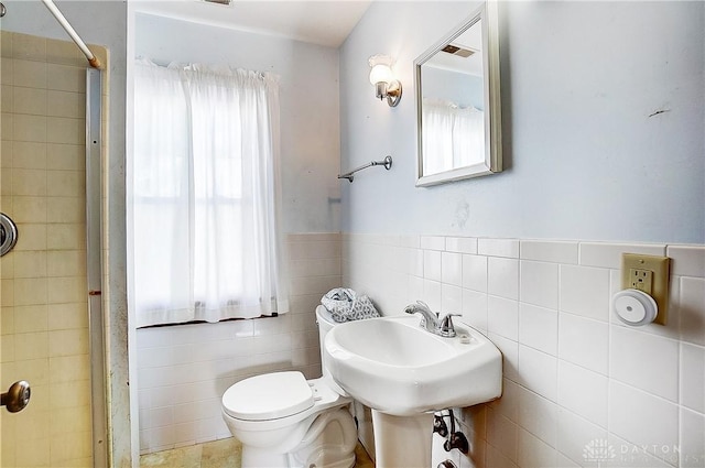 bathroom featuring tiled shower, a healthy amount of sunlight, toilet, and tile walls