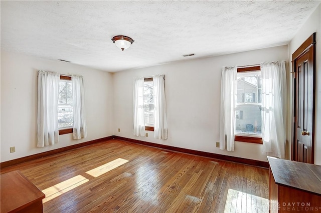 unfurnished room with hardwood / wood-style flooring, a healthy amount of sunlight, and a textured ceiling