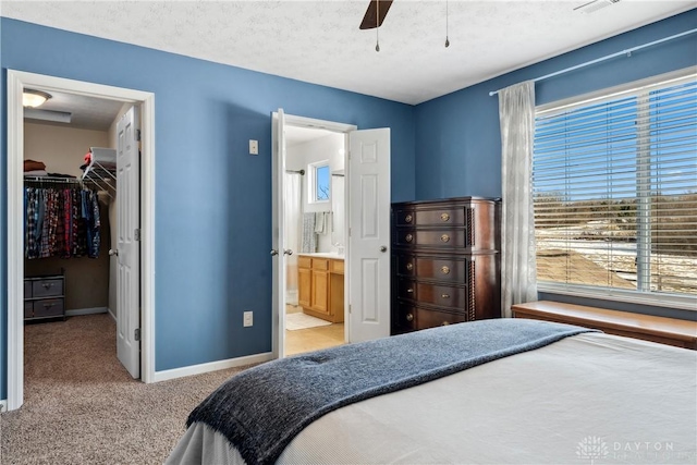 bedroom featuring a walk in closet, light colored carpet, a textured ceiling, ensuite bath, and a closet