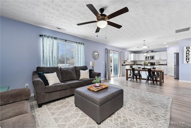 living room with ceiling fan, light hardwood / wood-style floors, and a textured ceiling