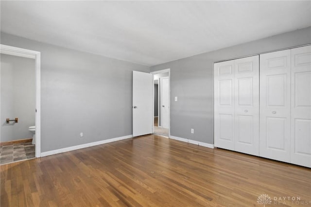 unfurnished bedroom with hardwood / wood-style floors, ensuite bath, and a closet