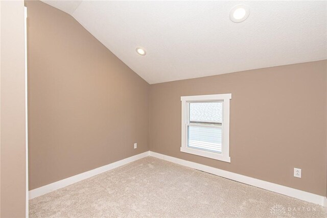 additional living space with vaulted ceiling, light carpet, and a textured ceiling