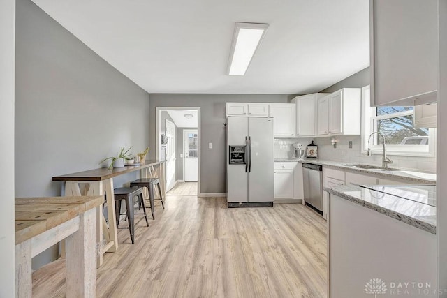 kitchen with refrigerator with ice dispenser, sink, dishwasher, light stone counters, and white cabinets