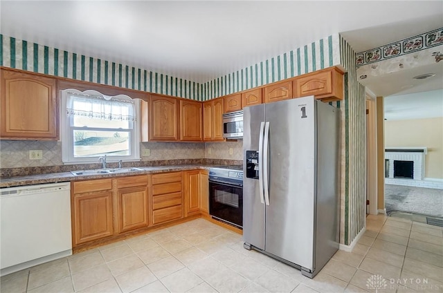 kitchen featuring appliances with stainless steel finishes, sink, decorative backsplash, light tile patterned floors, and a brick fireplace