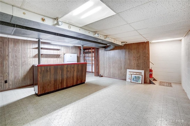 basement featuring white fridge and wood walls