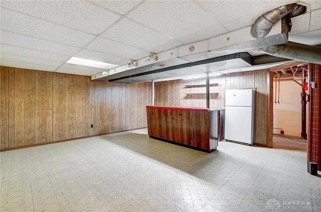 basement with bar, wood walls, a drop ceiling, and white fridge