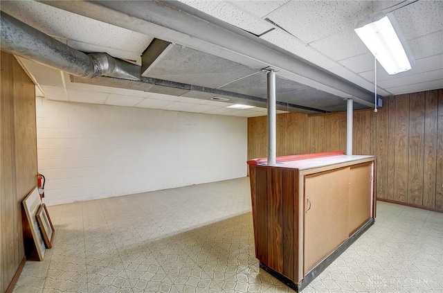 basement featuring bar area, a drop ceiling, and wood walls