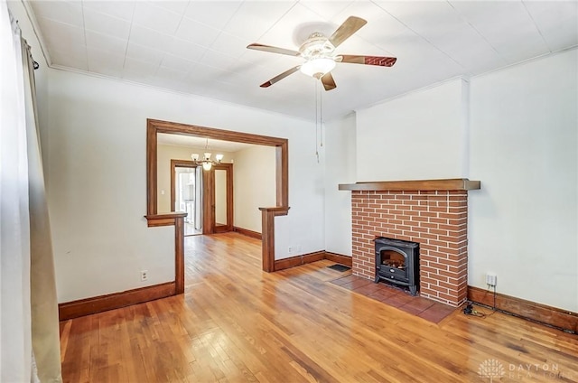 unfurnished living room featuring wood-type flooring, a wood stove, ceiling fan, and crown molding