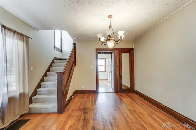 foyer entrance featuring a notable chandelier, crown molding, a textured ceiling, and light wood-type flooring