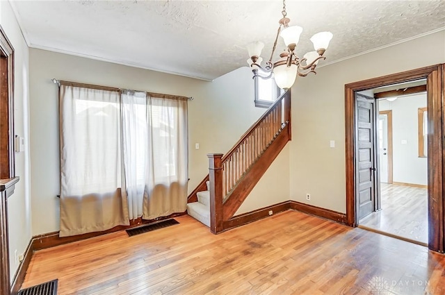 interior space with an inviting chandelier, ornamental molding, a textured ceiling, and light wood-type flooring