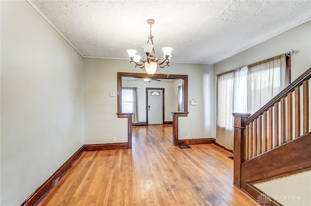 entrance foyer featuring crown molding, a textured ceiling, an inviting chandelier, and light hardwood / wood-style flooring