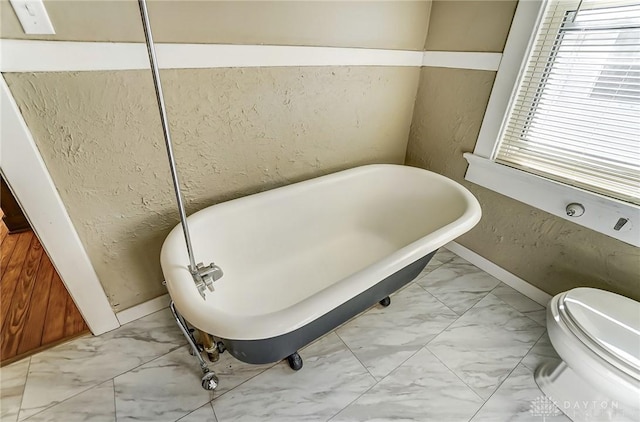 bathroom with a tub to relax in and toilet