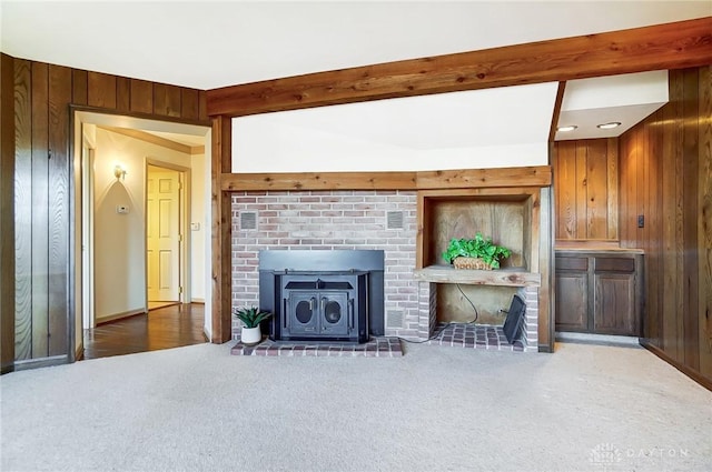 unfurnished living room featuring dark carpet, a wood stove, beamed ceiling, and wood walls