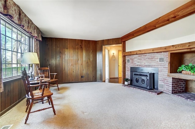 sitting room with beamed ceiling, wooden walls, carpet, and a wood stove