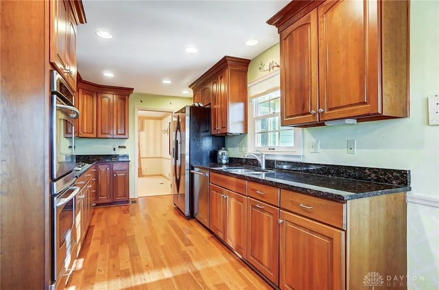 kitchen with stainless steel appliances, light hardwood / wood-style floors, sink, and dark stone countertops