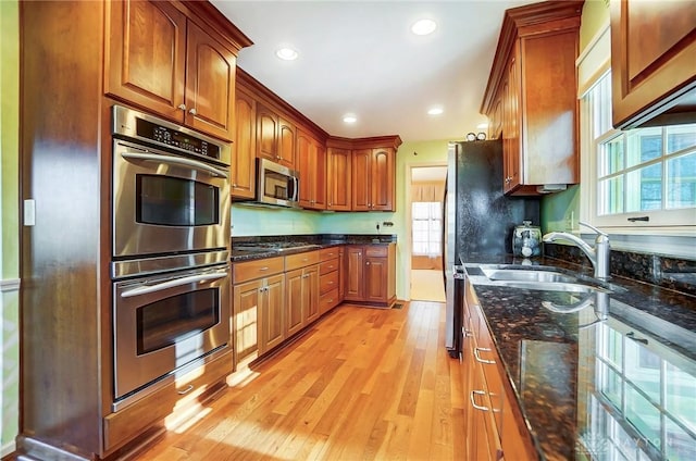 kitchen with appliances with stainless steel finishes, sink, light hardwood / wood-style flooring, and dark stone counters