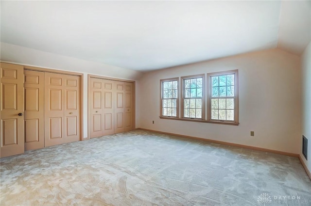 unfurnished bedroom featuring multiple closets, lofted ceiling, and light carpet