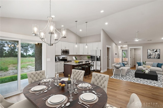 dining room featuring sink, ceiling fan with notable chandelier, high vaulted ceiling, and light hardwood / wood-style flooring