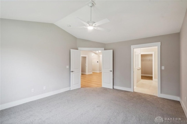 unfurnished bedroom featuring ceiling fan, light colored carpet, vaulted ceiling, and a walk in closet