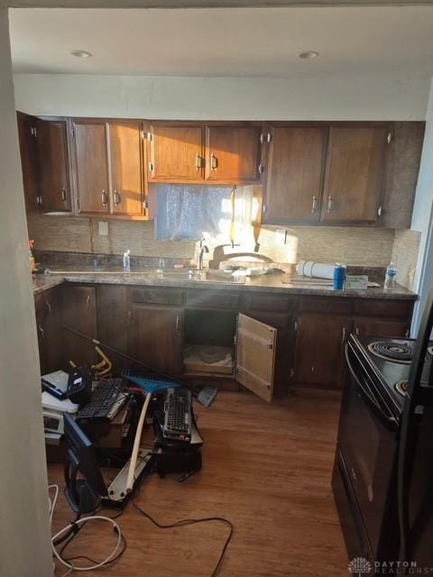 kitchen featuring dark wood-type flooring, stone countertops, black range with electric stovetop, and decorative backsplash